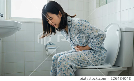 A woman in pajamas enduring stomach pain in the toilet 126484048