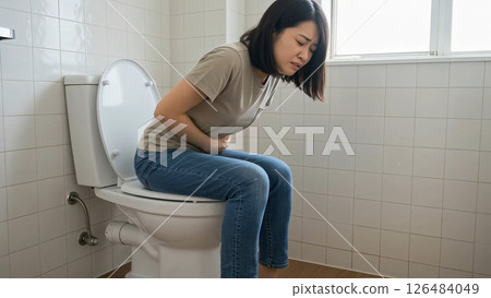 A woman in a T-shirt and jeans enduring stomach pain in the toilet 126484049