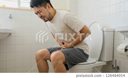 A bearded man in a white T-shirt endures stomach pain in the toilet A bearded man in a white T-shirt endures stomach pain in the toilet 126484054