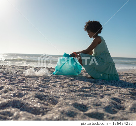 Collecting plastic waste on beach at sunset, African American woman promoting eco-awareness, copy sp 126484253