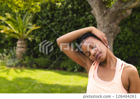 In garden, woman stretching neck, finding peaceful moment outside in nature, copy space 126484261
