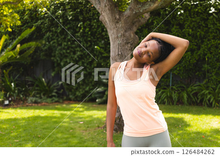Woman stretching neck in sunny garden, enjoying outdoor exercise and relaxation, copy space 126484262