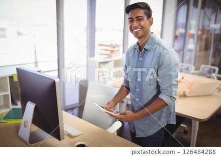 Smiling man using tablet in modern office, standing by desk with computer, copy space 126484288