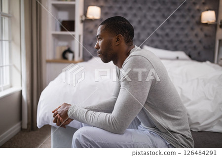 Contemplating life, African American man sitting on bed, gazing out window 126484291