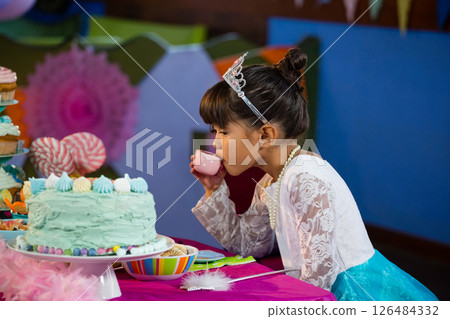 Young girl in princess dress sipping tea at colorful birthday party table, copy space 126484332