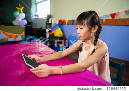 At kids' party, girl with tablet focusing on screen, colorful decorations around, copy space 126484335