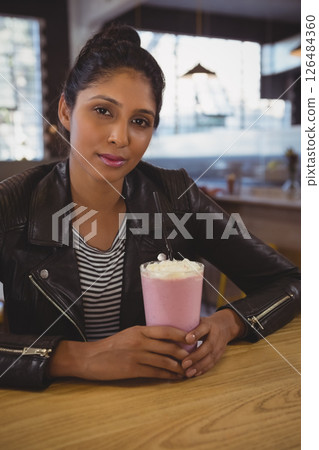 Woman enjoying strawberry milkshake at trendy cafe, wearing stylish leather jacket Woman enjoying strawberry milkshake at trendy cafe, wearing stylish leather jacket 126484360