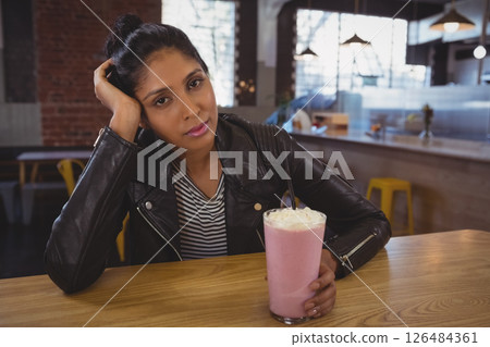 Woman in leather jacket enjoying strawberry milkshake at trendy cafe table 126484361