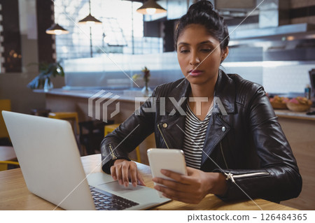 Young woman using smartphone and laptop in trendy cafe, concentrating on work 126484365