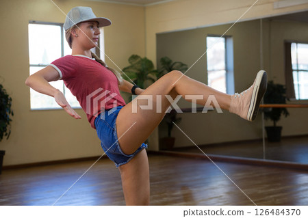 Young woman practicing dance moves in studio, wearing casual outfit and cap Young woman practicing dance moves in studio, wearing casual outfit and cap 126484370