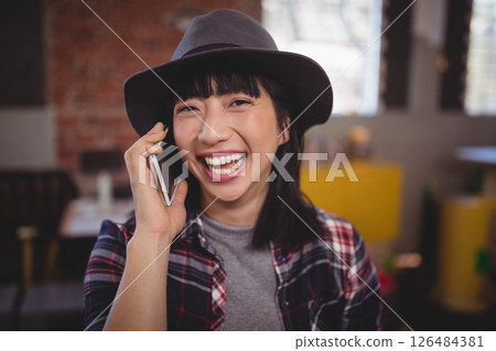 Smiling woman in hat talking on smartphone in cozy cafe, enjoying conversation Smiling woman in hat talking on smartphone in cozy cafe, enjoying conversation 126484381