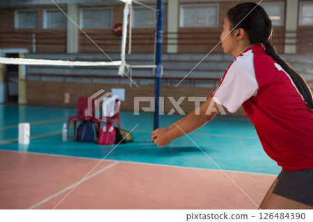 In school gym, girl in red jersey playing volleyball, focusing on game, copy space 126484390