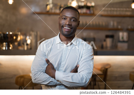 Smiling man in restaurant standing confidently with arms crossed, enjoying evening Smiling man in restaurant standing confidently with arms crossed, enjoying evening 126484391