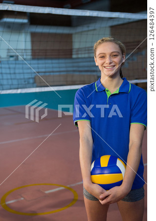 Teen girl holding volleyball, smiling confidently on indoor court, ready to play, copy space 126484397