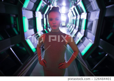 In futuristic corridor, confident woman standing with hands on hips, looking determined 126484401