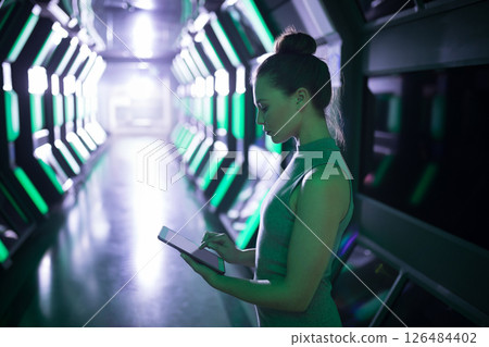Woman using tablet in futuristic office corridor, focused on digital tasks, copy space 126484402