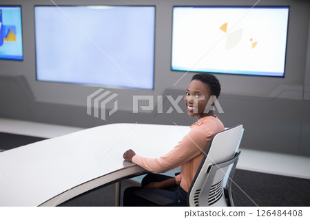 Smiling woman sitting at modern desk in high-tech office environment, copy space 126484408