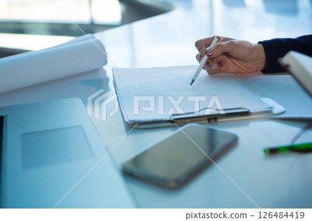 Hand writing on clipboard with smartphone and laptop on modern office desk, copy space Hand writing on clipboard with smartphone and laptop on modern office desk, copy space 126484419