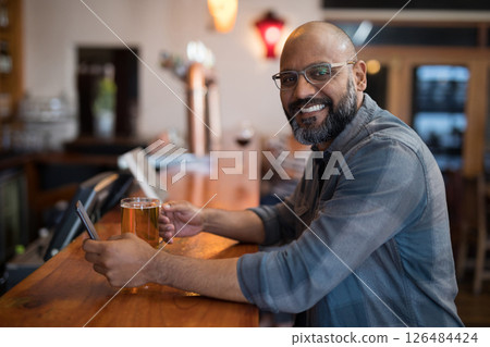 Smiling man enjoying beer and using smartphone at cozy bar counter, copy space Smiling man enjoying beer and using smartphone at cozy bar counter, copy space 126484424
