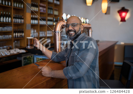 Smiling man enjoying beer at bar, holding smartphone, feeling relaxed and happy Smiling man enjoying beer at bar, holding smartphone, feeling relaxed and happy 126484428