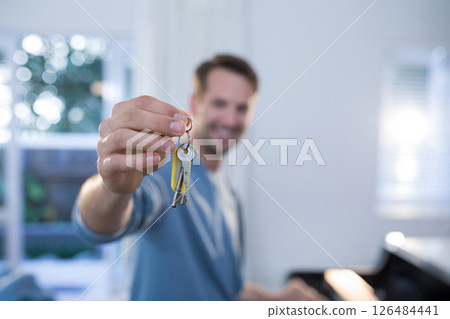 Smiling man holding keys in bright living room, celebrating new home, copy space 126484441