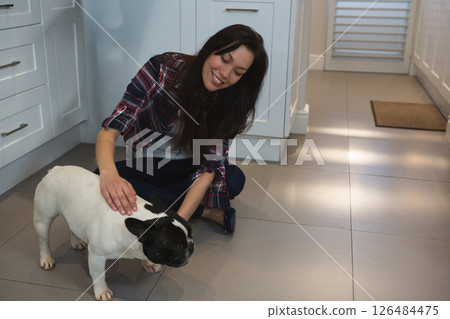 Smiling woman petting French Bulldog on kitchen floor at home, copy space 126484475