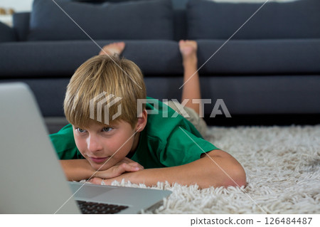 Young boy watching laptop on carpet at home, focused and relaxed, copy space 126484487