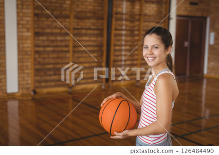 Smiling girl holding basketball in school gym, ready for practice, copy space 126484490