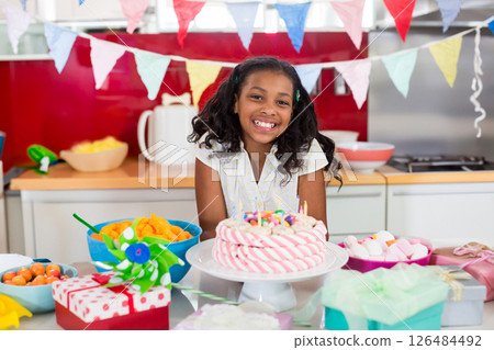 Smiling girl celebrating birthday at home with cake and colorful decorations 126484492