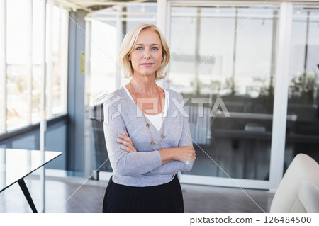 Confident businesswoman standing in modern office, arms crossed, looking determined 126484500