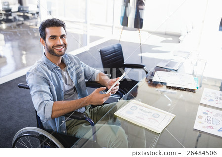 Smiling man in wheelchair using smartphone at modern office desk, copy space Smiling man in wheelchair using smartphone at modern office desk, copy space 126484506