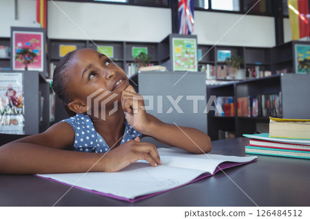 In school library, young girl thinking while writing in notebook, feeling inspired, copy space 126484512
