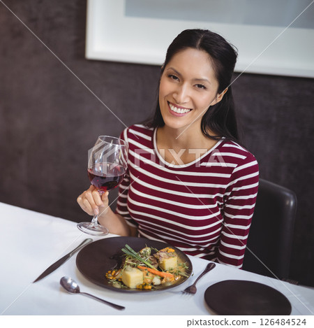 Woman enjoying wine and gourmet meal at restaurant, smiling happily at camera 126484524