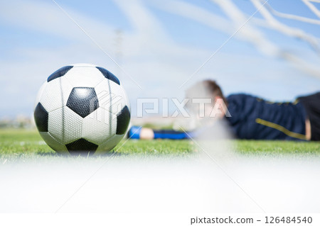 Soccer ball on field with player in background reaching for goal, copy space 126484540