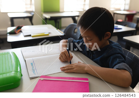 In school, young boy writing in notebook at desk, concentrating on task, copy space In school, young boy writing in notebook at desk, concentrating on task, copy space 126484543