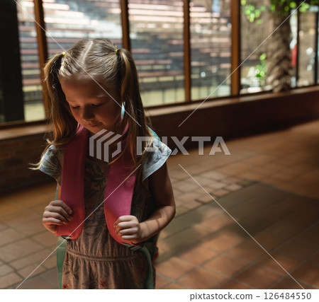 Young girl with backpack exploring school hallway, looking curious and thoughtful, copy space 126484550