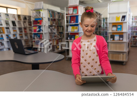 Girl in school library using tablet, smiling and exploring digital content, copy space Girl in school library using tablet, smiling and exploring digital content, copy space 126484554