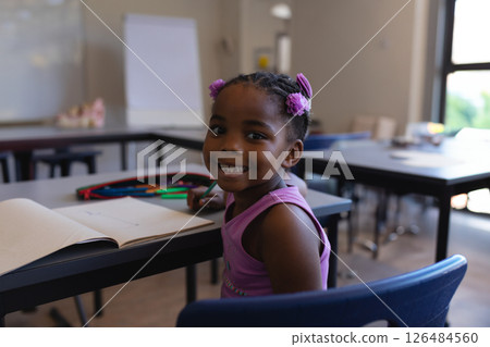 In school, smiling girl sitting at desk with open notebook in classroom In school, smiling girl sitting at desk with open notebook in classroom 126484560