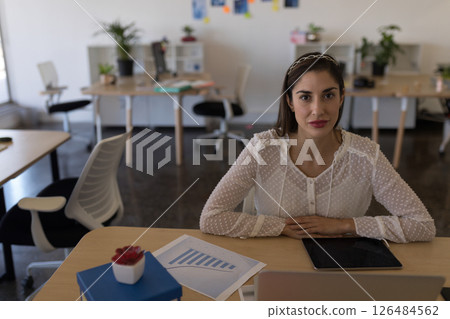 Businesswoman in office sitting at desk with tablet and financial charts, copy space 126484562