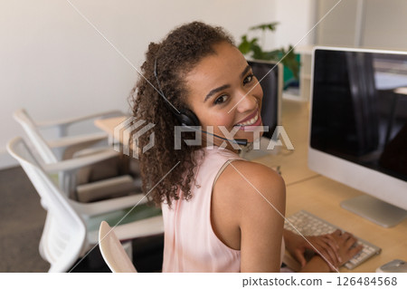 Smiling woman using headset and computer at office, providing customer support 126484568