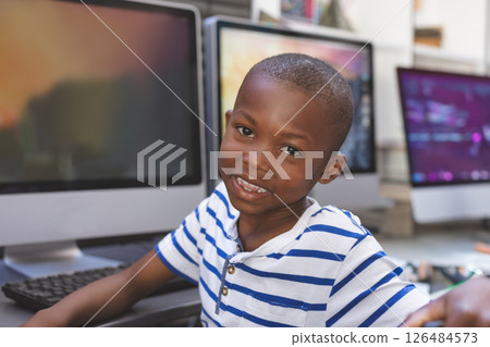 In school, smiling boy in striped shirt sitting at computer desk 126484573