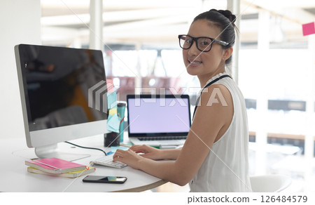 Asian woman working at desk with computer and laptop, smiling confidently, copy space 126484579