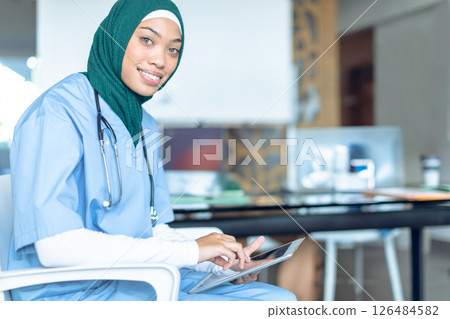 Healthcare professional in scrubs using tablet in hospital, smiling confidently, copy space 126484582