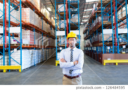 Warehouse manager in hard hat standing confidently among shelves of goods, copy space Warehouse manager in hard hat standing confidently among shelves of goods, copy space 126484595