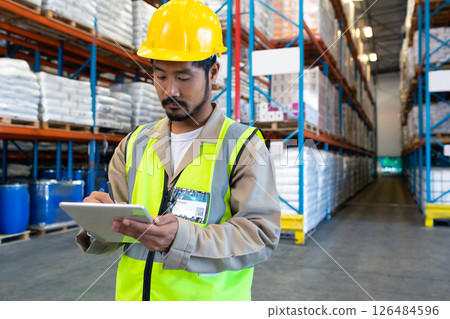 Warehouse worker in safety vest using tablet for inventory management, copy space 126484596