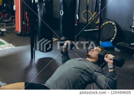 Man lifting dumbbells on bench in gym, focusing on strength training, copy space 126484608