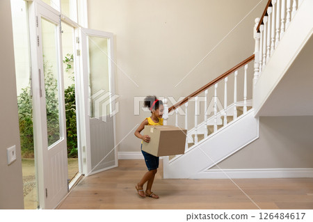 Young girl carrying cardboard box in hallway, moving into new home, copy space 126484617