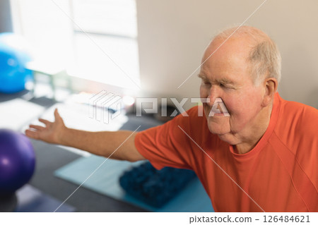 Senior man practicing yoga on mat, smiling and stretching arms in fitness studio, copy space 126484621