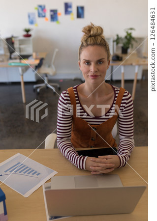 Businesswoman in office smiling confidently at camera with laptop and chart Businesswoman in office smiling confidently at camera with laptop and chart 126484631