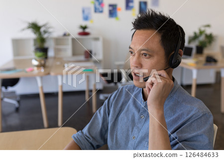Asian man using headset working in modern office, engaging in conversation, copy space 126484633